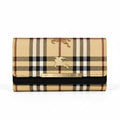 A Burberry wallet in the iconic beige, brown, and black check pattern, featuring a gold-tone metal plaque with the brand name and a gold equestrian logo on the front flap.
