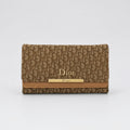 A Dior wallet in the brand's signature brown and beige Oblique monogram canvas, featuring a tan leather trim and a gold-tone metal bar with 'Dior' branding.