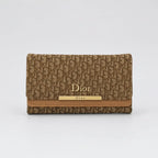 A Dior wallet in the brand's signature brown and beige Oblique monogram canvas, featuring a tan leather trim and a gold-tone metal bar with 'Dior' branding.