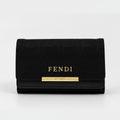 A black Fendi wallet featuring the brand name in gold lettering and a gold bar accent on the front, set against a plain light gray background.