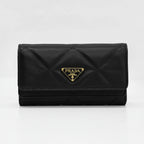 A black Prada quilted wallet with a gold-tone triangular logo plaque on the front, set against a plain light gray background.