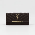 A dark brown quilted leather wallet by Yves Saint Laurent, featuring a gold-tone metal YSL logo and brand plaque on the front flap, set against a plain light gray background.