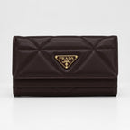 A dark brown Prada quilted leather wallet with a gold-tone triangular logo plaque on the front, set against a plain light gray background.