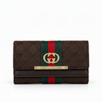 Gucci monogram canvas wallet in dark brown with a green and red web stripe, gold-tone interlocking G logo, and a gold-tone metal bar engraved with 'GUCCI' on a white background.