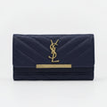 A navy blue quilted leather wallet with a gold-tone YSL monogram and a gold bar accent on the front, set against a plain white background.